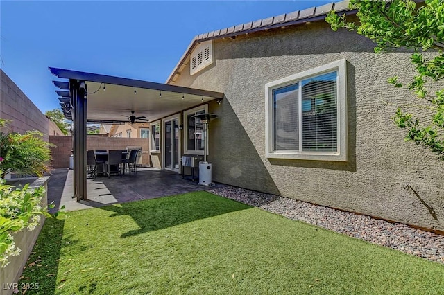 rear view of property with stucco siding, a fenced backyard, a patio area, a ceiling fan, and a yard