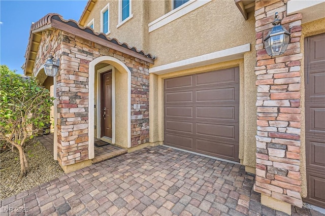 property entrance with a garage, stucco siding, and stone siding