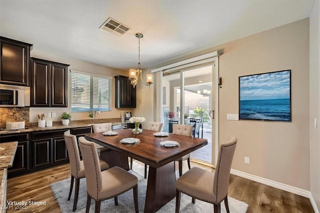 dining area featuring baseboards, visible vents, an inviting chandelier, and wood finished floors