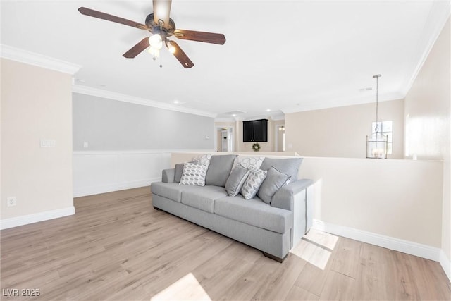 living area with light wood-style flooring, ceiling fan with notable chandelier, a wainscoted wall, recessed lighting, and ornamental molding