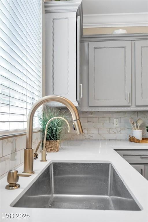 room details with crown molding, a sink, light countertops, gray cabinets, and backsplash