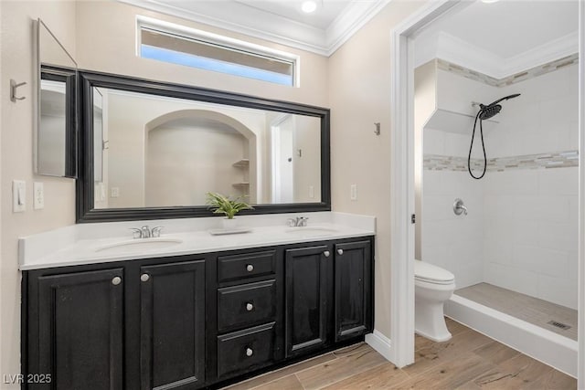 bathroom with a tile shower, toilet, ornamental molding, and a sink