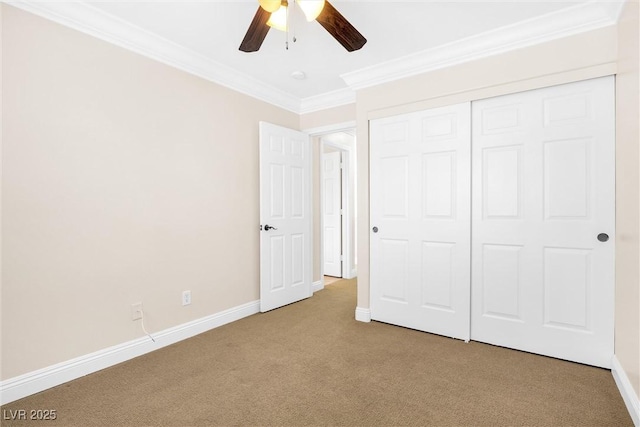 unfurnished bedroom with carpet floors, ornamental molding, a closet, baseboards, and a ceiling fan