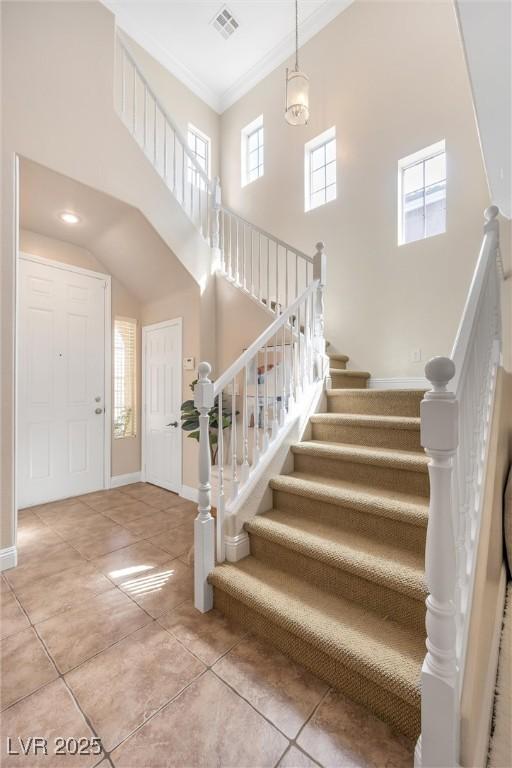 stairway featuring baseboards, tile patterned flooring, a high ceiling, and visible vents
