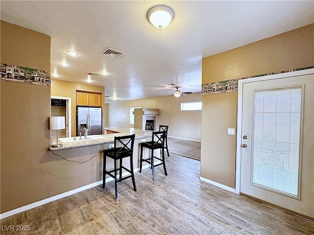 5704 Burdel St, Las Vegas, NV 89149 - kitchen featuring visible vents, light wood-style floors, a breakfast bar area, ceiling fan, and stainless steel refrigerator with ice dispenser