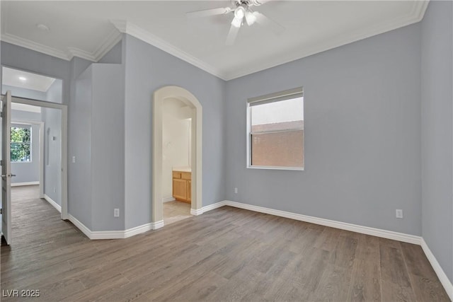 spare room with crown molding, arched walkways, ceiling fan, and wood finished floors