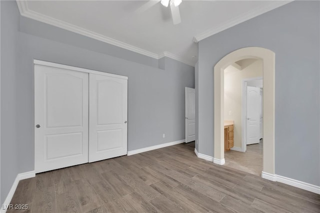 unfurnished bedroom with crown molding, arched walkways, baseboards, and wood finished floors
