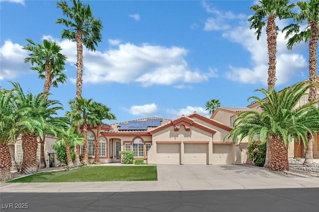 mediterranean / spanish-style home featuring a garage, stucco siding, roof mounted solar panels, concrete driveway, and a tile roof