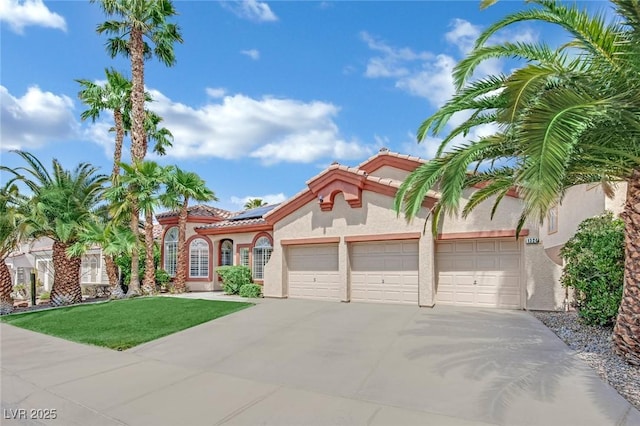 mediterranean / spanish-style house featuring an attached garage, solar panels, stucco siding, and concrete driveway