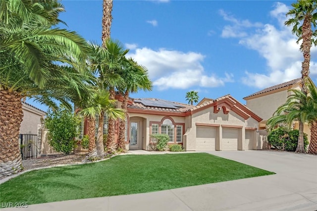 mediterranean / spanish house with driveway, a garage, roof mounted solar panels, a front lawn, and stucco siding