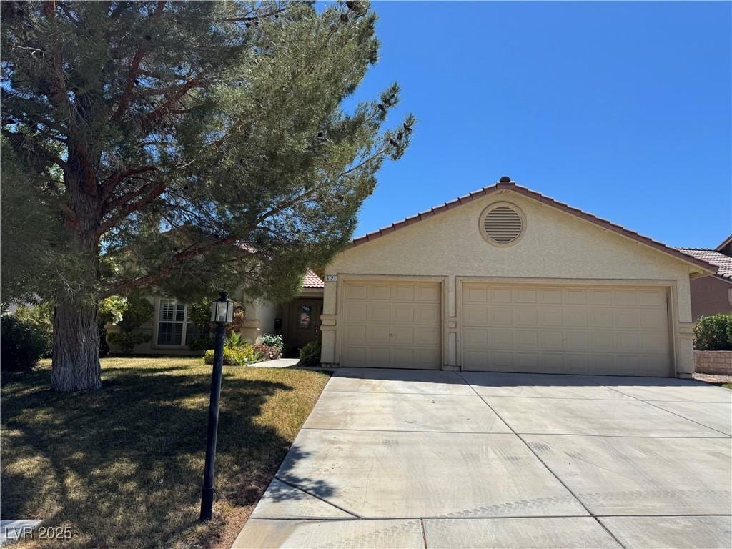 ranch-style house with an attached garage, a tile roof, stucco siding, a front yard, and concrete driveway