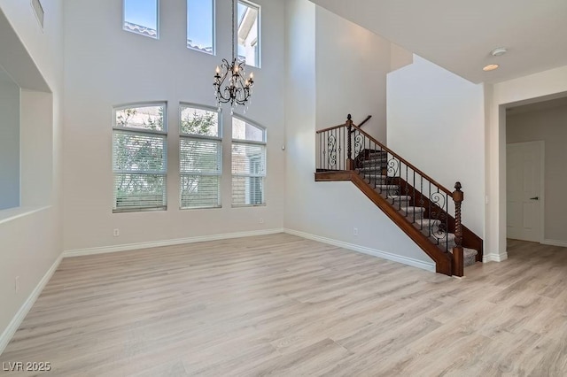 unfurnished living room featuring healthy amount of natural light, light wood finished floors, a chandelier, stairs, and a high ceiling