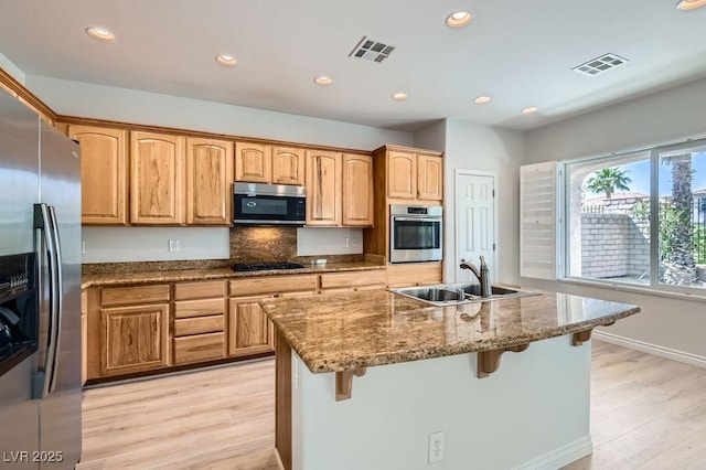 kitchen with appliances with stainless steel finishes, a sink, stone counters, light wood-style floors, and recessed lighting