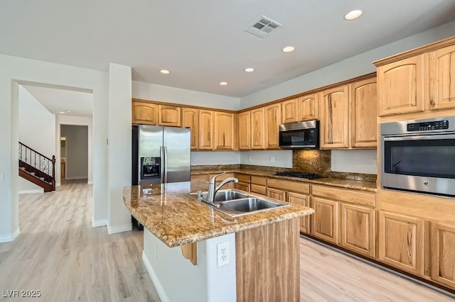 kitchen featuring stainless steel appliances, a sink, light wood-type flooring, a center island with sink, and recessed lighting