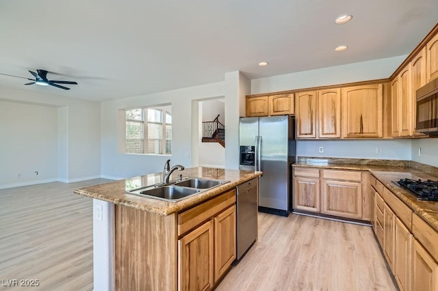 kitchen featuring stainless steel appliances, a sink, light wood finished floors, a kitchen island with sink, and ceiling fan