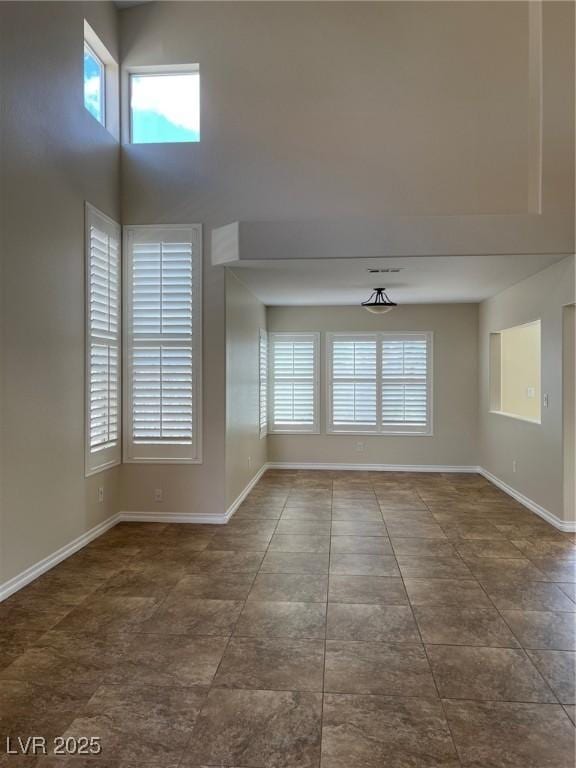 tiled empty room with baseboards and a high ceiling