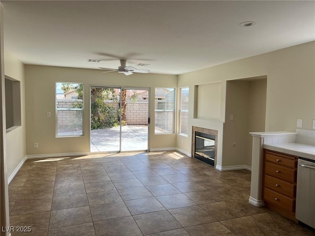 unfurnished living room with a tiled fireplace, visible vents, baseboards, and ceiling fan
