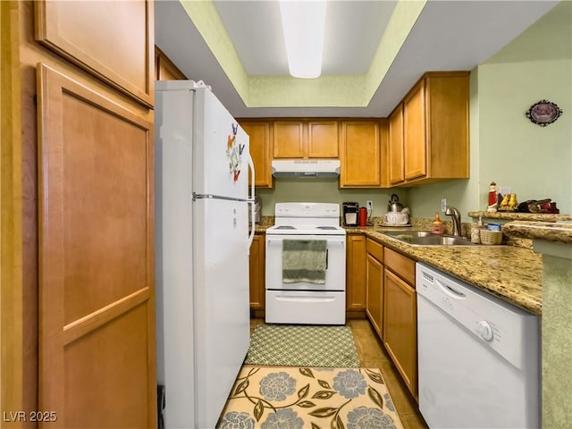 kitchen featuring under cabinet range hood, white appliances, light tile patterned flooring, a sink, and brown cabinets