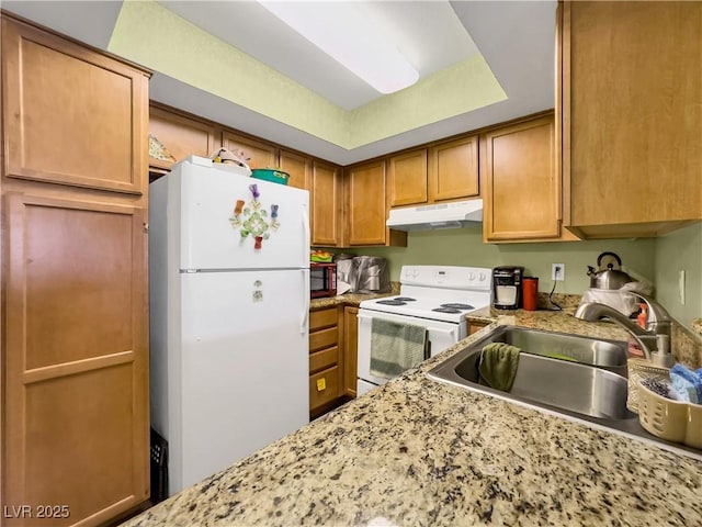 kitchen with light stone countertops, under cabinet range hood, white appliances, a sink, and brown cabinets