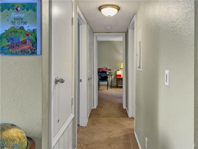 hallway featuring light carpet, a textured wall, and baseboards