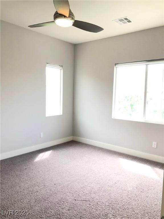 carpeted empty room with baseboards, a ceiling fan, and visible vents