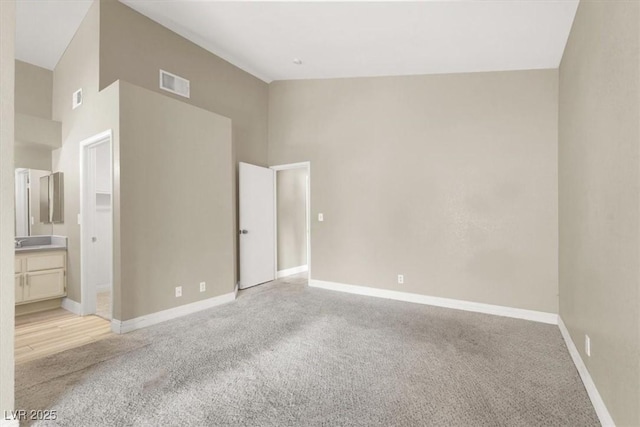 unfurnished bedroom with baseboards, visible vents, light carpet, and a towering ceiling