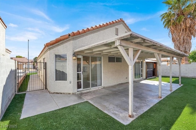rear view of house with a tiled roof, a gate, fence, a yard, and stucco siding