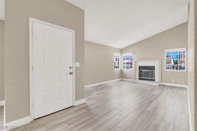 unfurnished living room featuring a glass covered fireplace, baseboards, light wood finished floors, and high vaulted ceiling