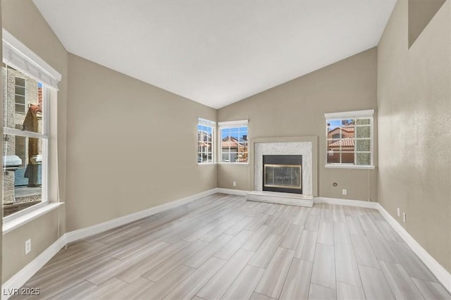 unfurnished living room with baseboards, vaulted ceiling, a glass covered fireplace, and wood finished floors