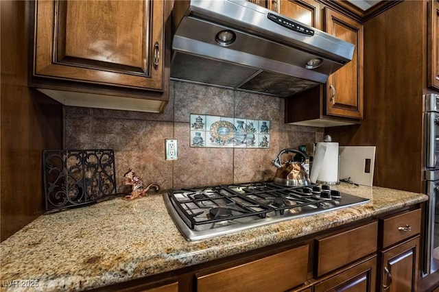 kitchen with light stone counters, tasteful backsplash, stainless steel appliances, and extractor fan