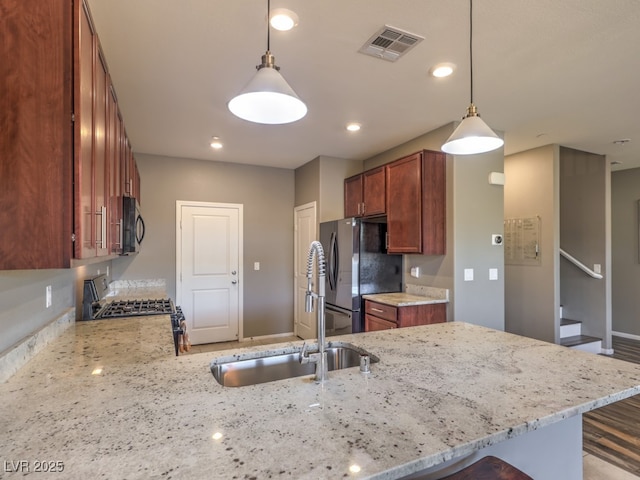 kitchen featuring gas range, black microwave, visible vents, a sink, and freestanding refrigerator