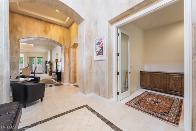 corridor featuring arched walkways, baseboards, and a tray ceiling