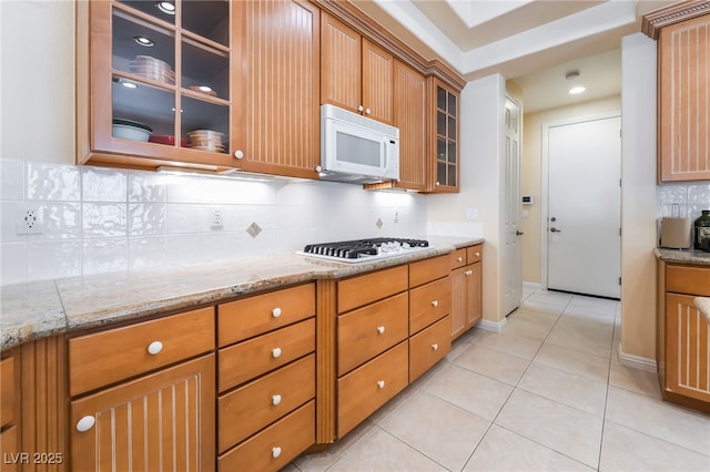 kitchen with white appliances, glass insert cabinets, light stone countertops, tasteful backsplash, and light tile patterned floors