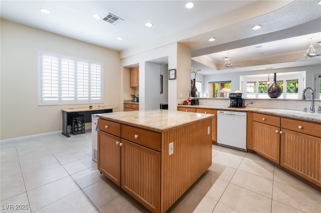 kitchen with a kitchen island, visible vents, white dishwasher, light stone countertops, and a sink