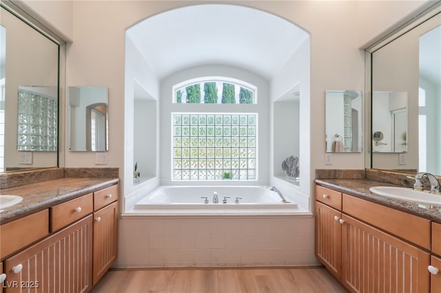 full bathroom with a garden tub, a sink, two vanities, and wood finished floors