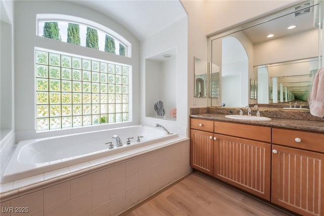 full bath with vanity, a garden tub, and wood finished floors