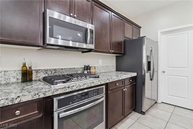 kitchen with appliances with stainless steel finishes, dark brown cabinets, light tile patterned floors, and light stone counters