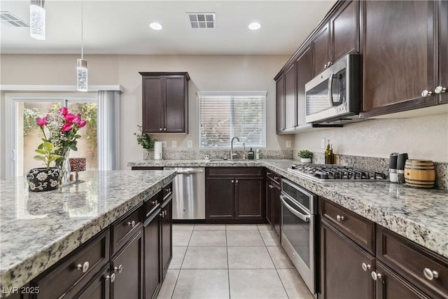 kitchen with stainless steel appliances, a sink, dark brown cabinets, light tile patterned floors, and light stone countertops