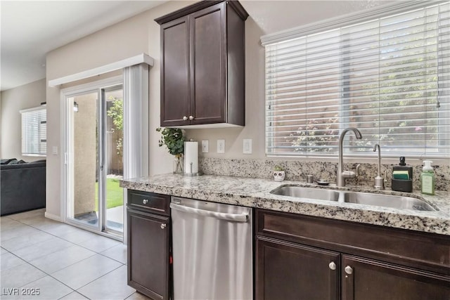 kitchen featuring stainless steel dishwasher, a sink, dark brown cabinets, light tile patterned floors, and light stone counters