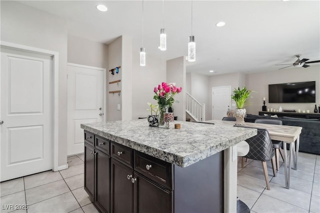 kitchen with light tile patterned flooring, a ceiling fan, hanging light fixtures, open floor plan, and a kitchen island