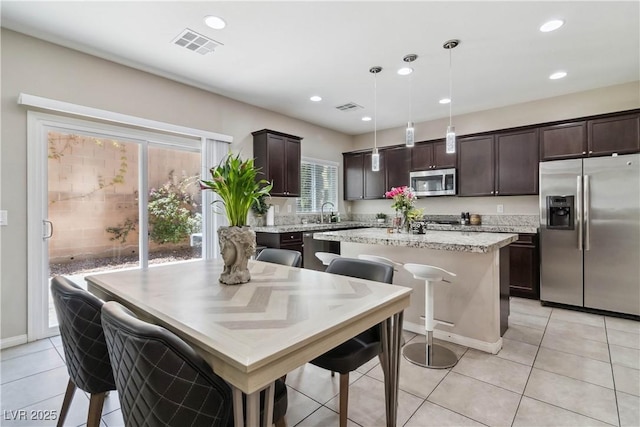 kitchen with stainless steel appliances, dark brown cabinets, a kitchen island, light tile patterned floors, and recessed lighting