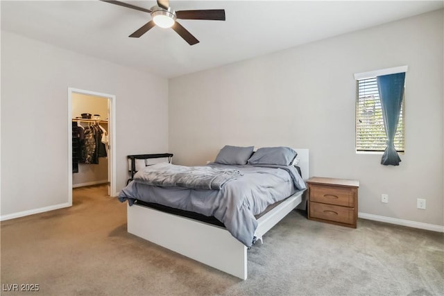 bedroom featuring light colored carpet, a walk in closet, baseboards, a ceiling fan, and a closet