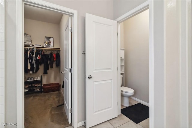 bathroom featuring toilet, a spacious closet, baseboards, and tile patterned flooring