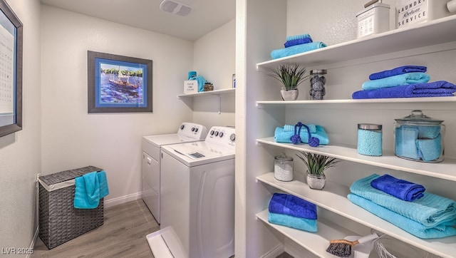 washroom with laundry area, visible vents, washing machine and dryer, wood finished floors, and baseboards