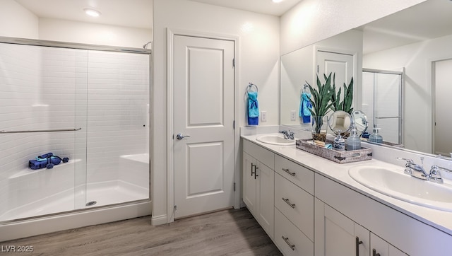 bathroom with wood finished floors, a sink, a stall shower, and double vanity