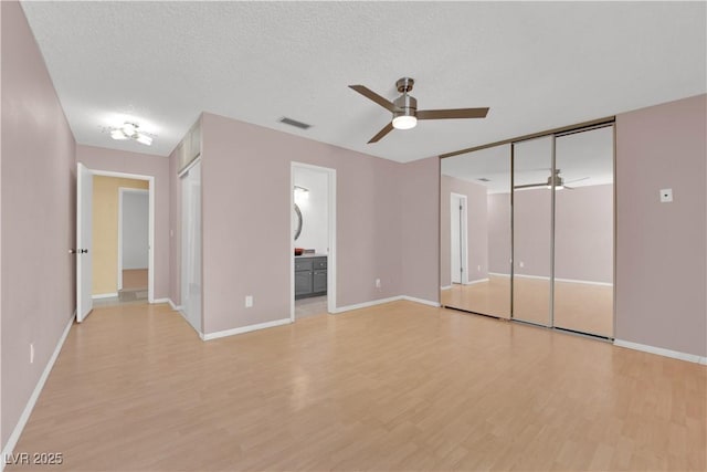 unfurnished bedroom featuring ensuite bath, baseboards, visible vents, and light wood-style floors