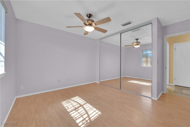 unfurnished bedroom with wood finished floors, a ceiling fan, a closet, visible vents, and baseboards