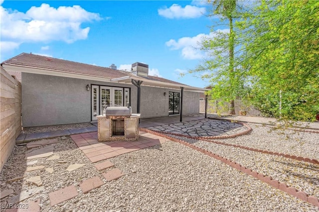 back of property with french doors, a patio, stucco siding, a fenced backyard, and a chimney