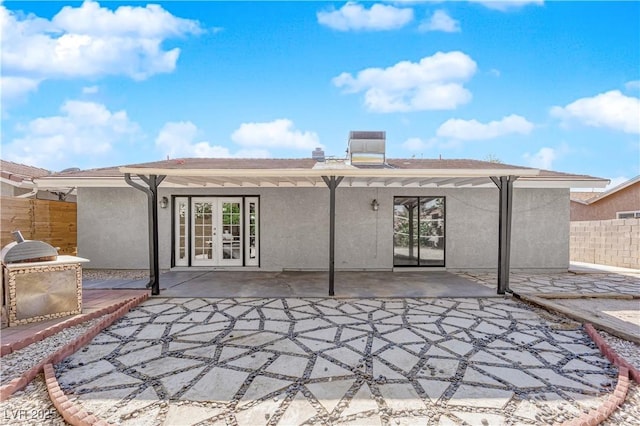 rear view of house with stucco siding, french doors, fence, and a patio