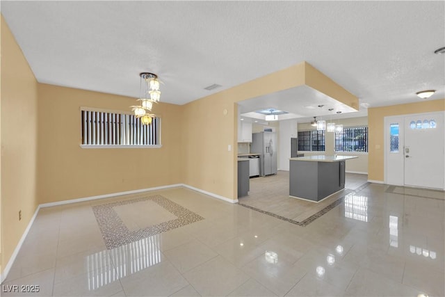 unfurnished living room with an inviting chandelier, baseboards, and light tile patterned flooring